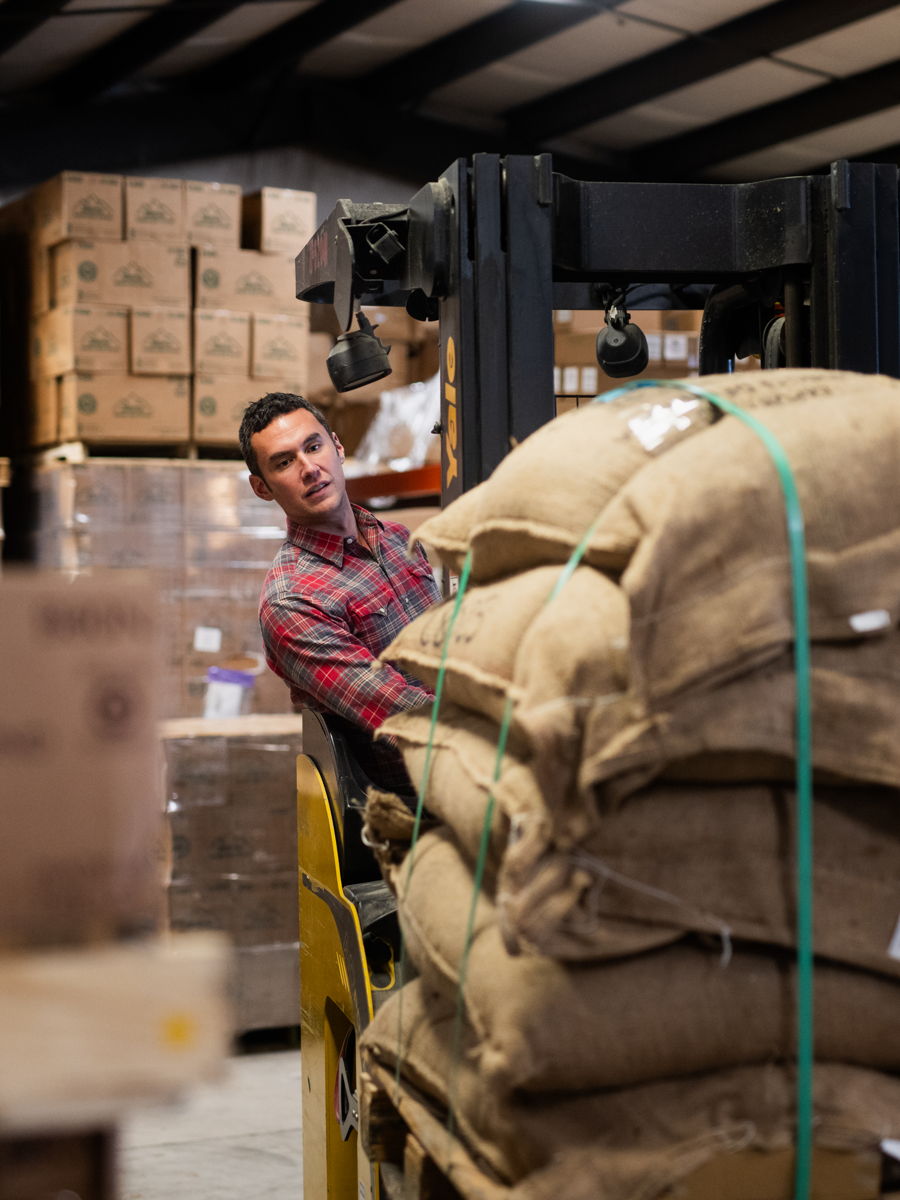 Burlap sacks of green coffee stacked high in the roastery&rsquo;s green-coffee room