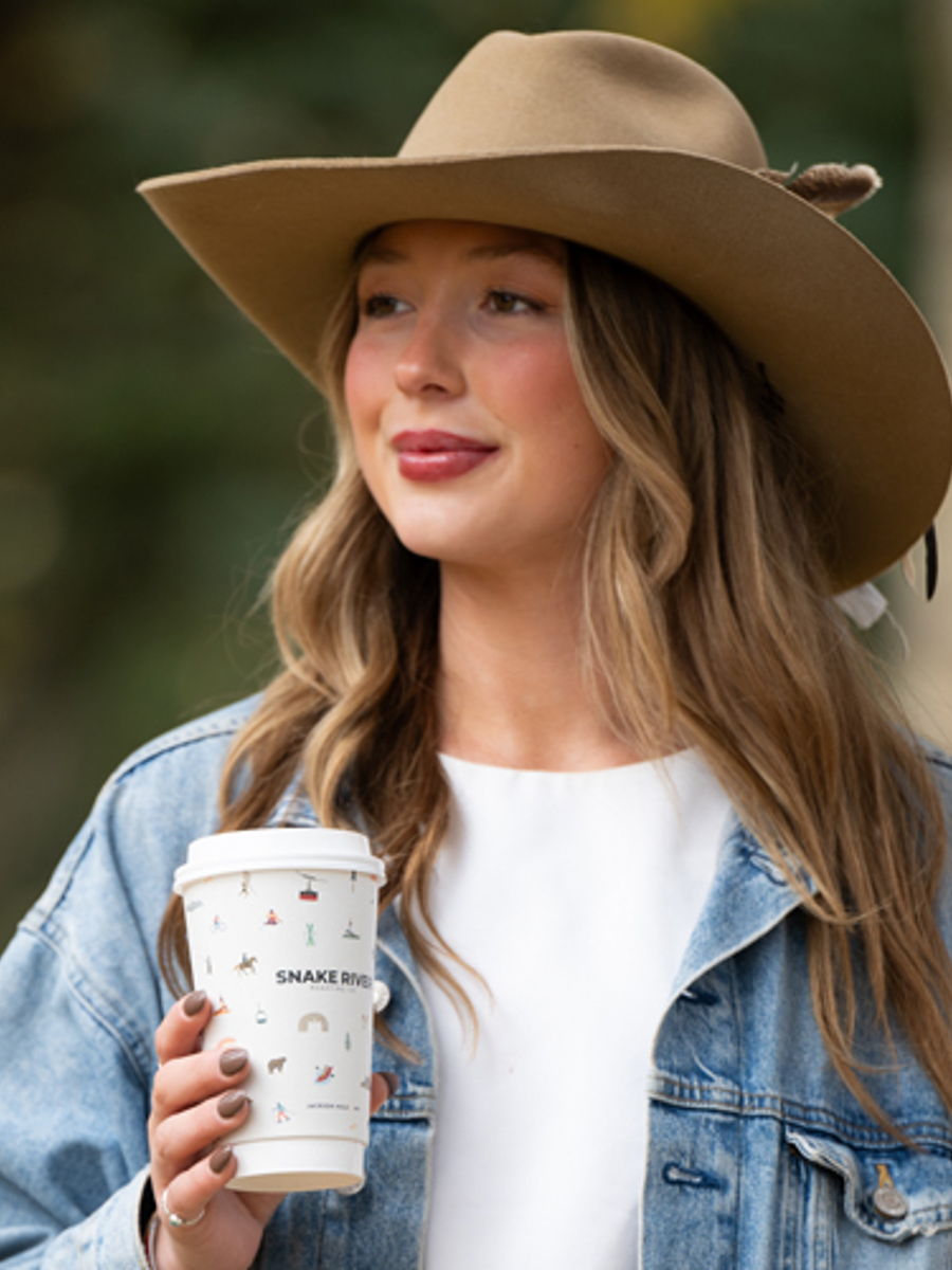 Ellie Crown in a wide-brim hat holding a patterned Snake River Roasting Co. cup