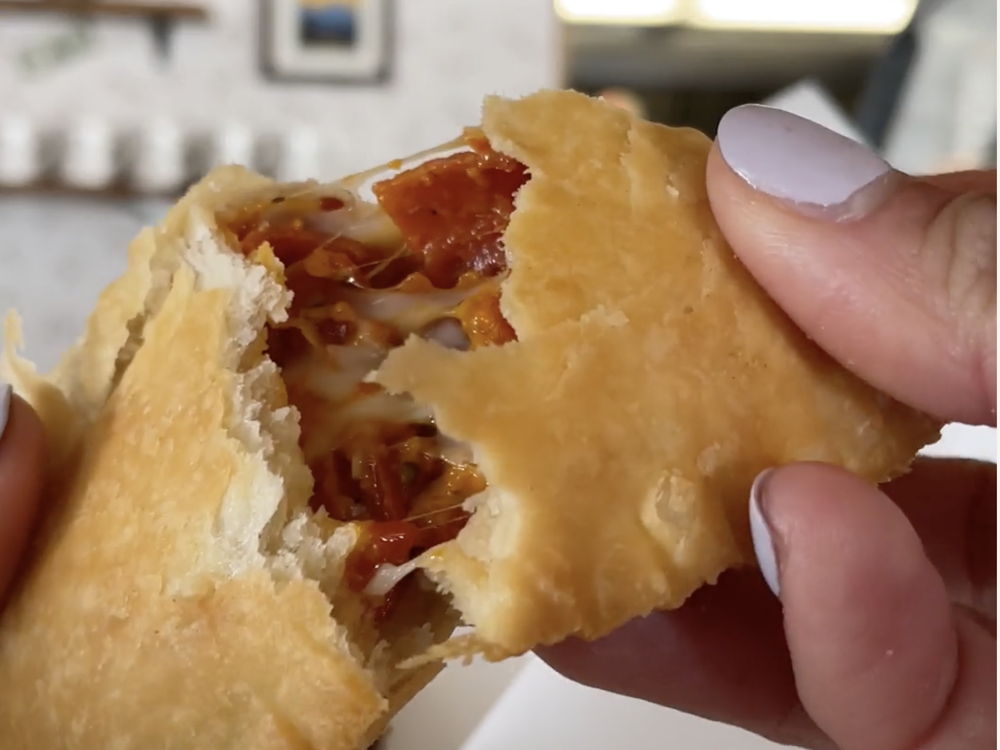 An empanada in hand with the first bite taken and the filling showing